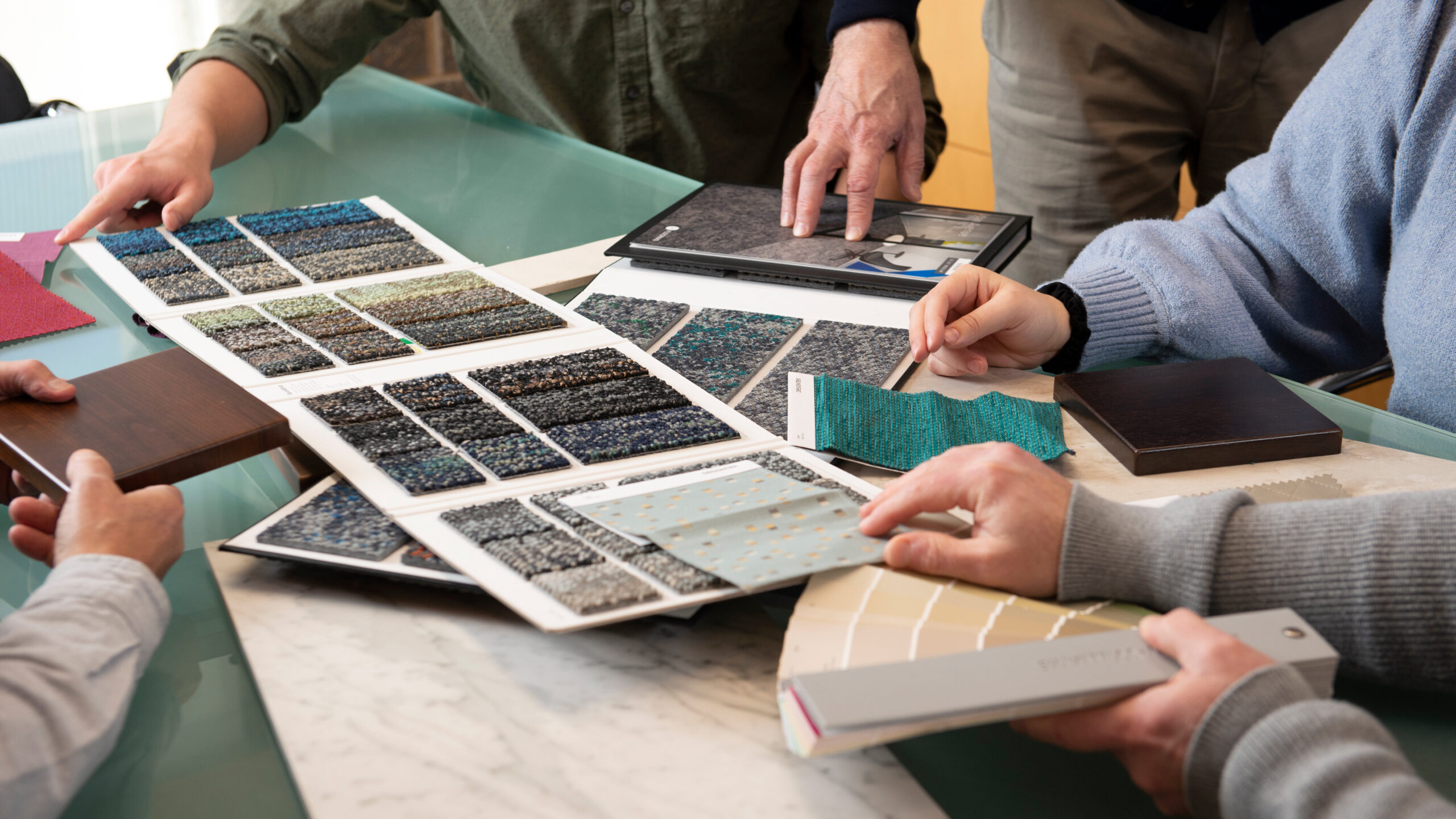 Designers are looking through different interior design materials to help develop a consistent interior brand for a client. They are looking at carpet samples, counter top samples, and paint samples. 